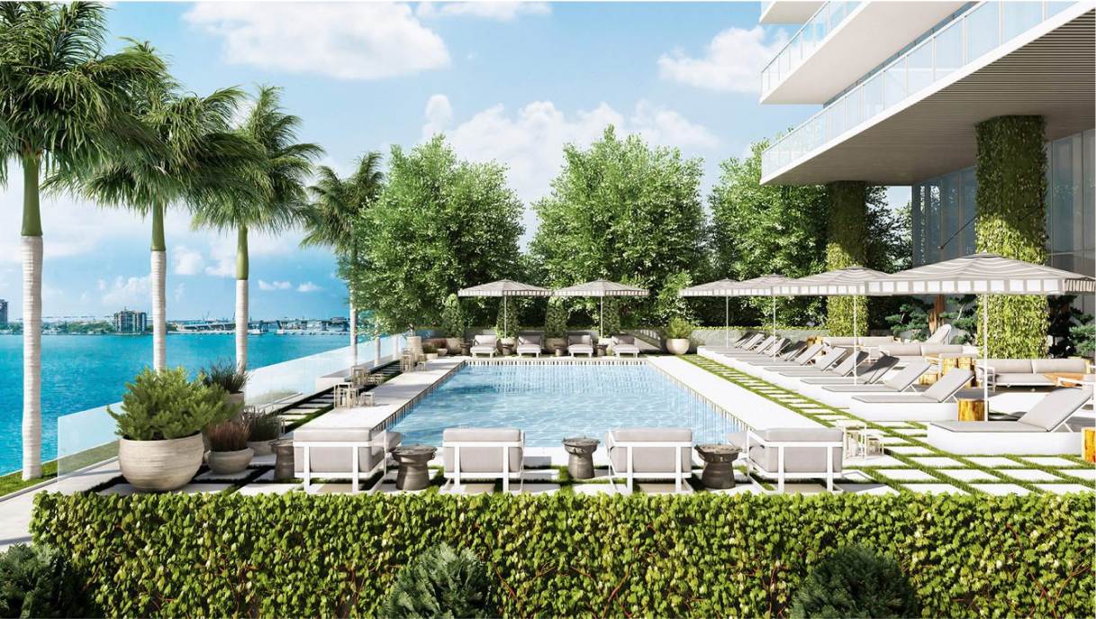 A luxurious outdoor pool area overlooking a waterfront, surrounded by lush greenery and palm trees.